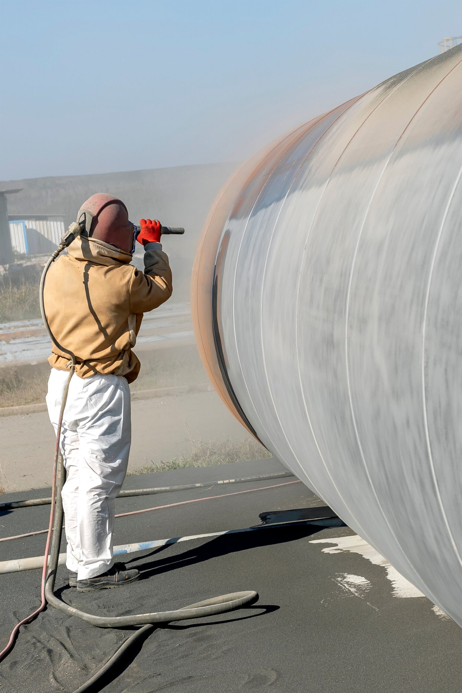 The sandblaster is sanding to steel pipe material. Sand blasting is also known as abrasive blasting, which is a generic term for the process of smoothing, shaping and cleaning a hard surface.